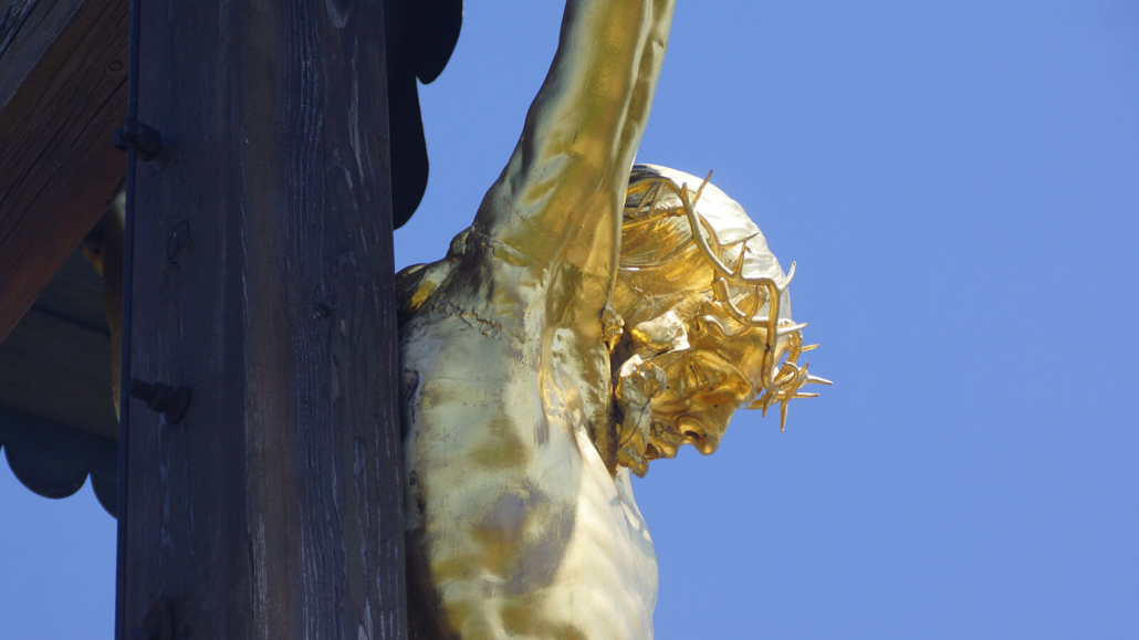 Eine goldfarbene Jesusskulptur an einem dunklen Holzkreuz