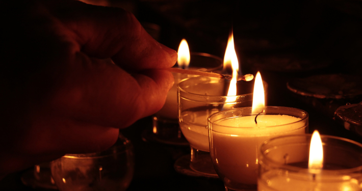 Eine Hand zündet Opferlichter in einer Kirche an