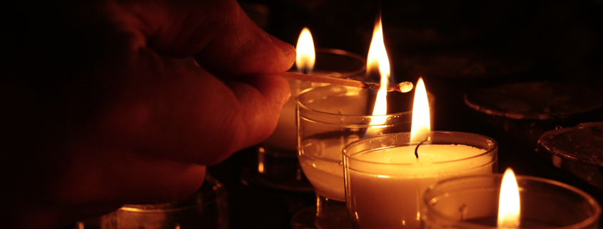 Eine Hand zündet Opferlichter in einer Kirche an