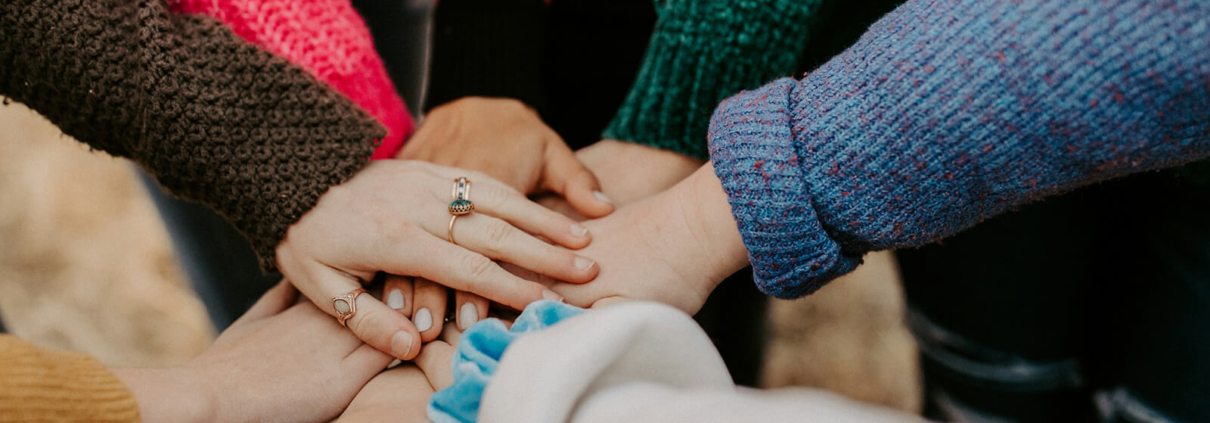 Acht Menschen in Winterkleidung legen die Hände übereinander